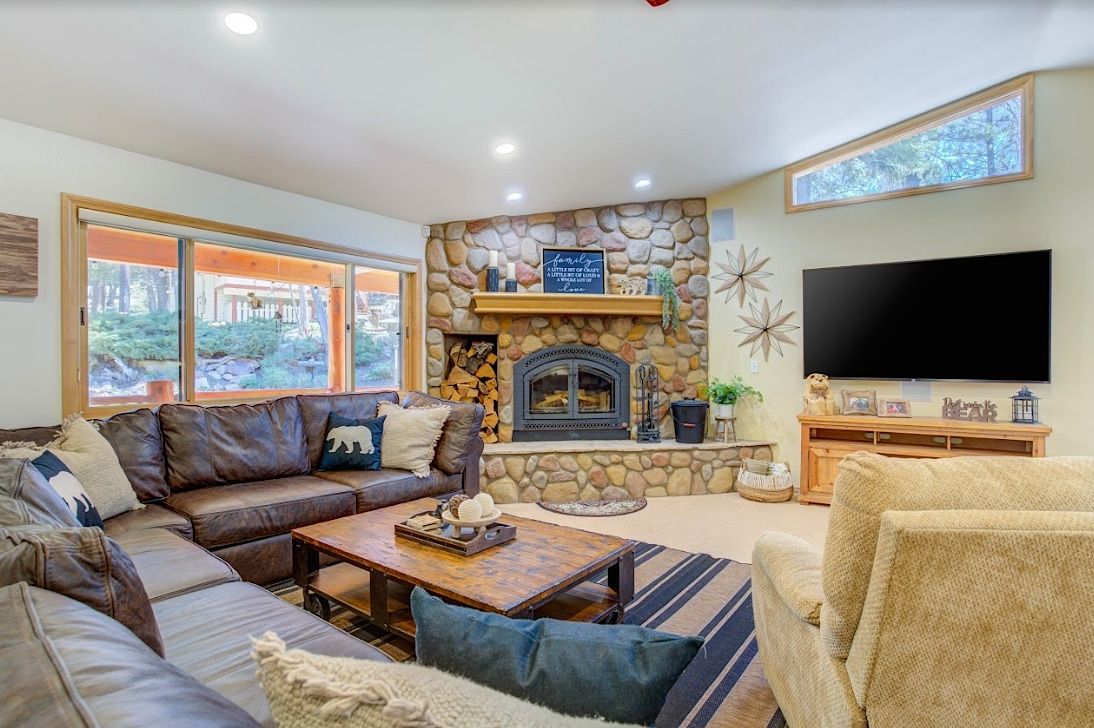 Living room with stone fireplace, leather sectional sofa, and large TV