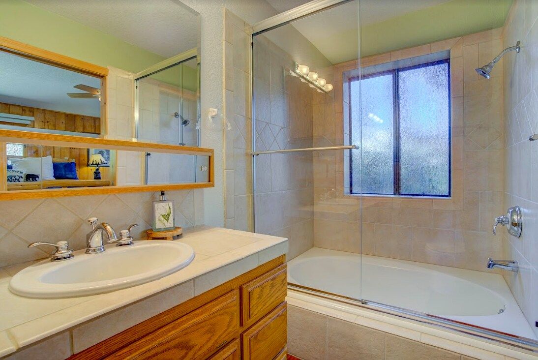 Bathroom with tiled shower-tub combo, vanity, and large mirror