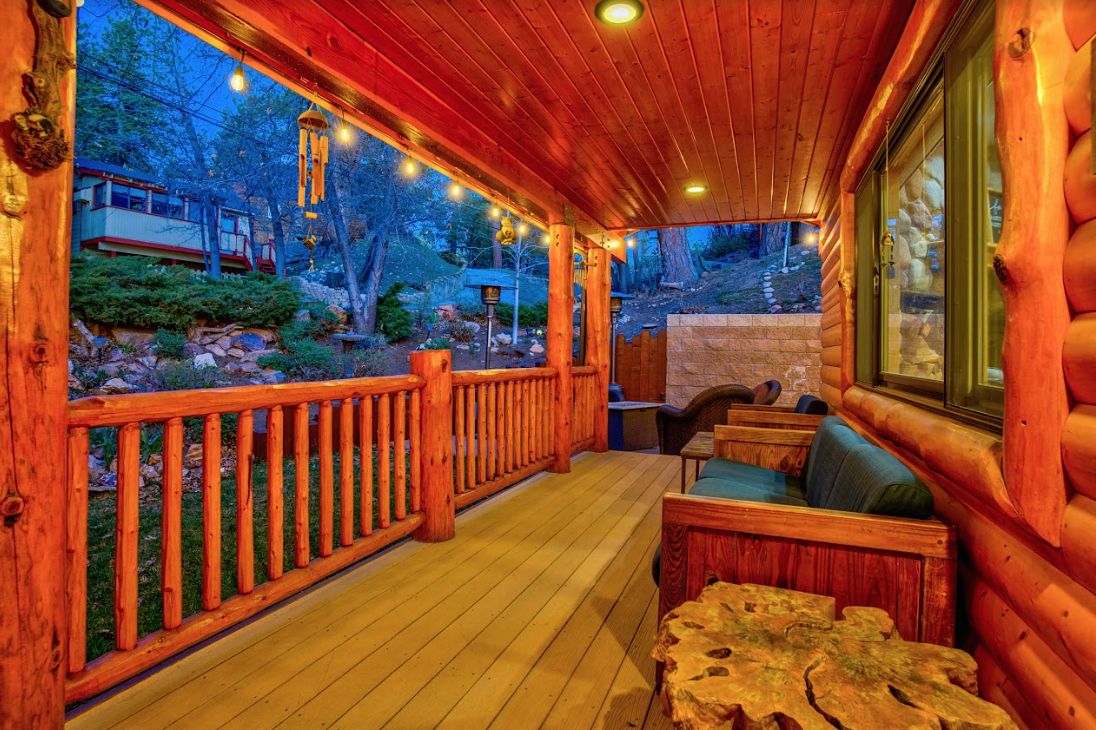 Covered front porch at twilight with string lights, log railings, and bench seating