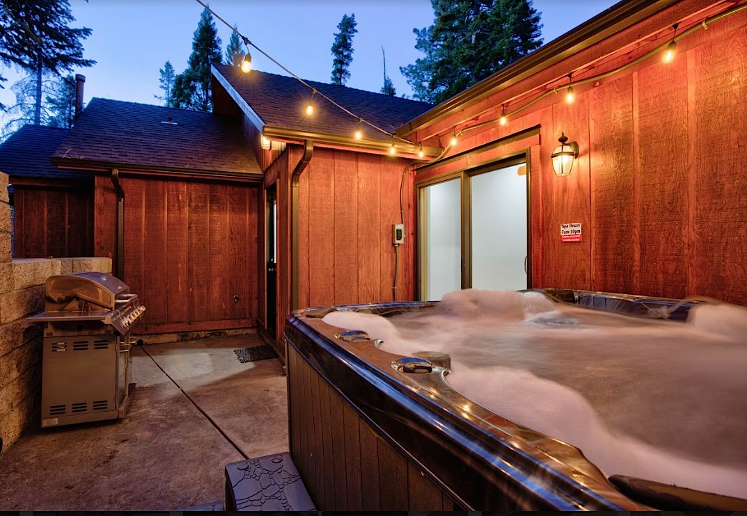 Private hot tub steaming on the patio at dusk with string lights and BBQ grill