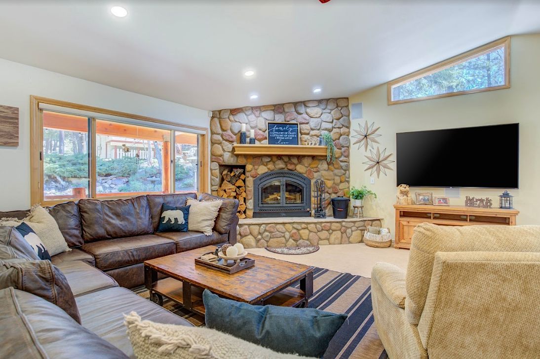 Living room with stone fireplace, leather sectional sofa, and wall-mounted TV