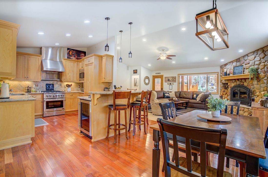Open-concept kitchen and living room with maple cabinets, stone fireplace, and dining area