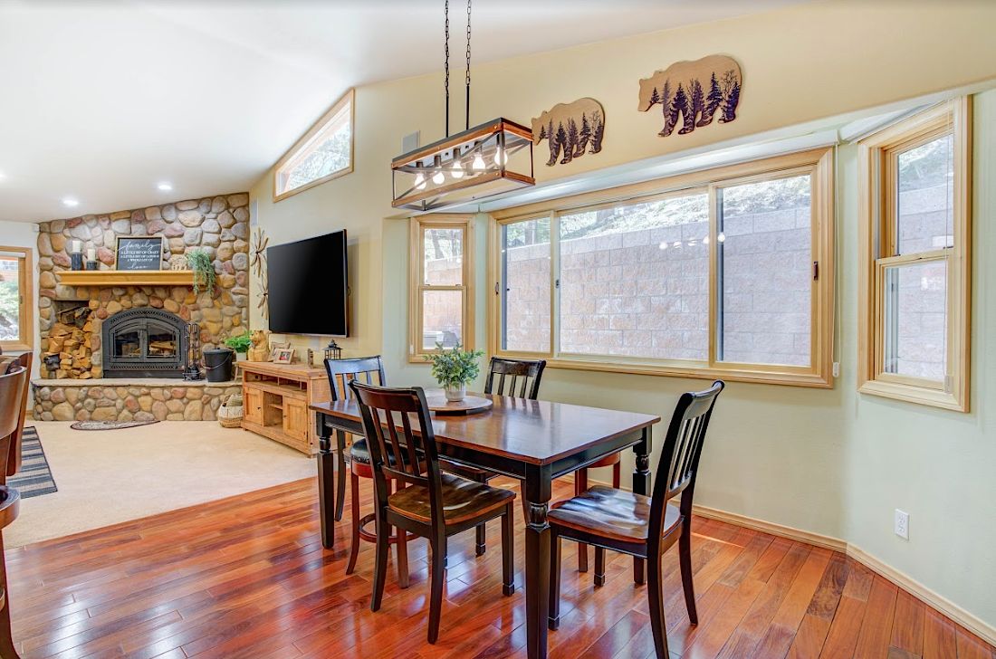 Dining room with stone fireplace, bear wall art, and large windows overlooking the trees