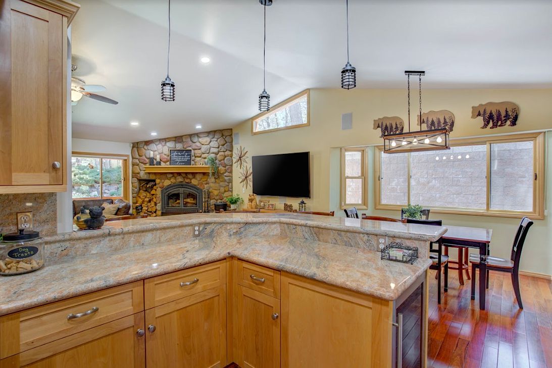 Kitchen bar with granite counters overlooking the living room with stone fireplace, TV, and dining area