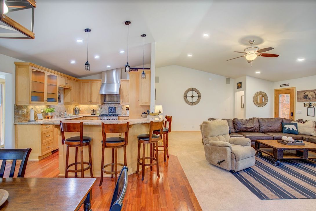 Open kitchen island with bar stools flowing into the living room with leather sectional and recliner