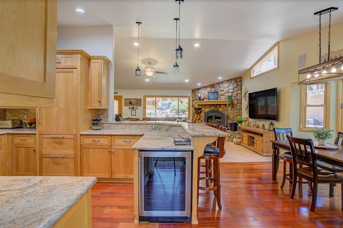 Kitchen island with built-in wine fridge and bar stools, living room with stone fireplace beyond
