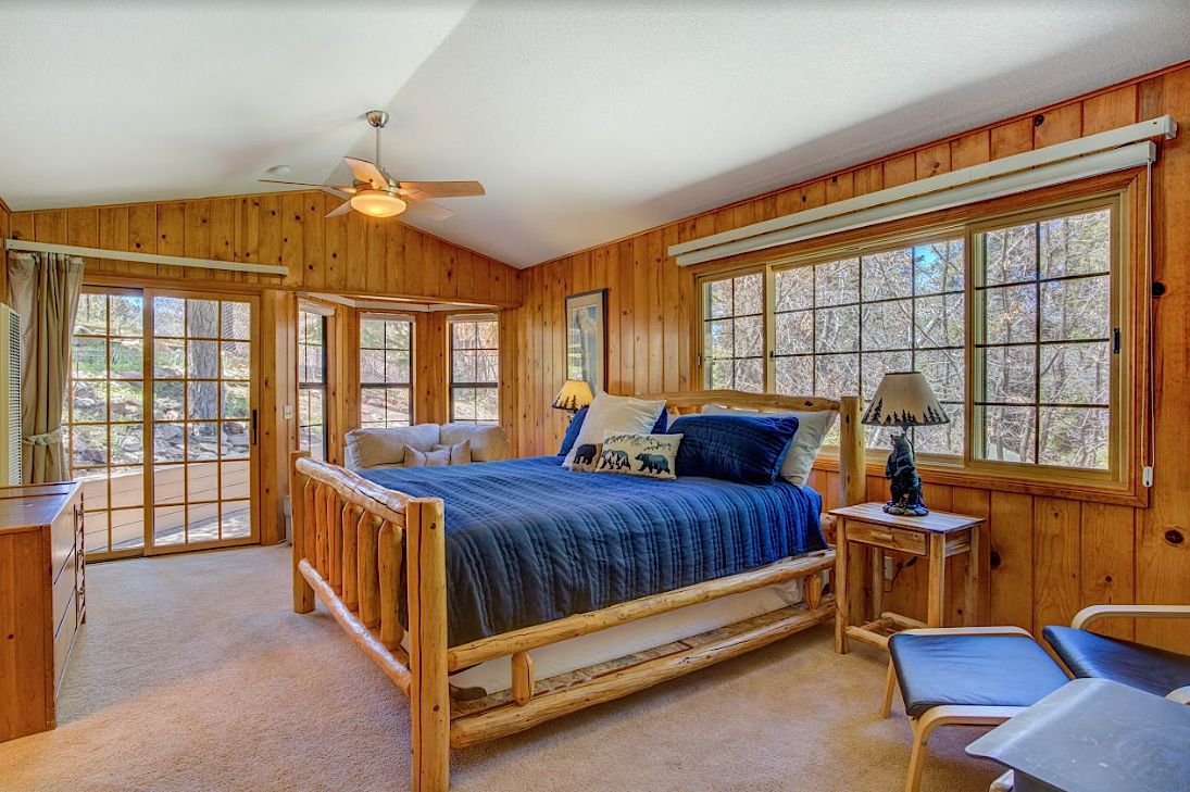 Master bedroom with log bed frame, blue bedding, wood-paneled walls, and patio door to the deck
