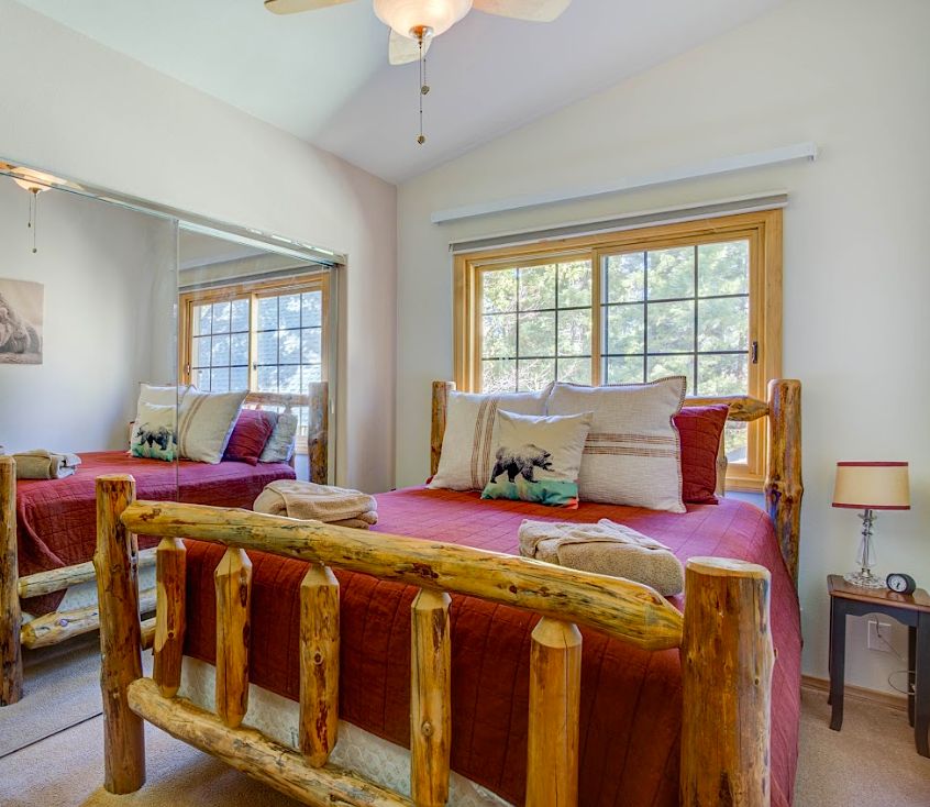 Bedroom with log bed frame, red bedding, mirrored closet doors, and window overlooking the pines
