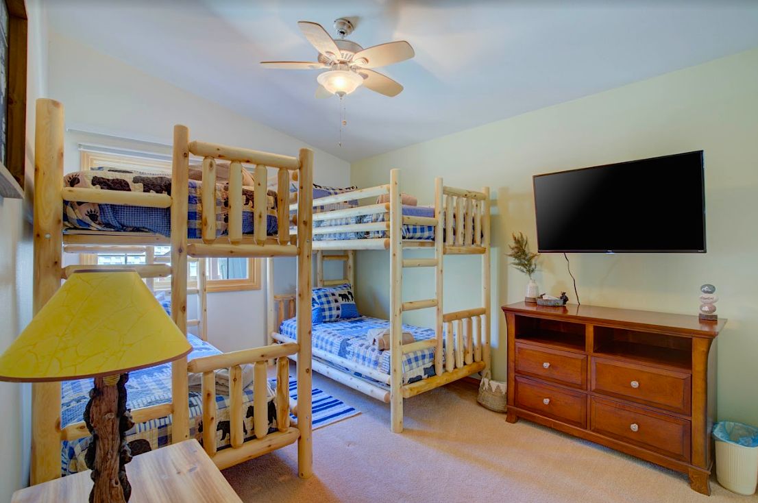 Bunk bedroom with two log bunk beds, wall-mounted TV, and dresser