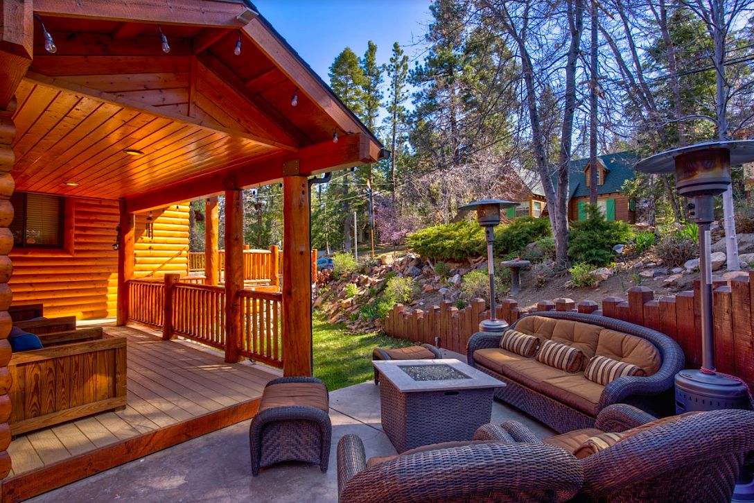 Covered deck with wicker lounge seating, fire pit table, heaters, and string lights