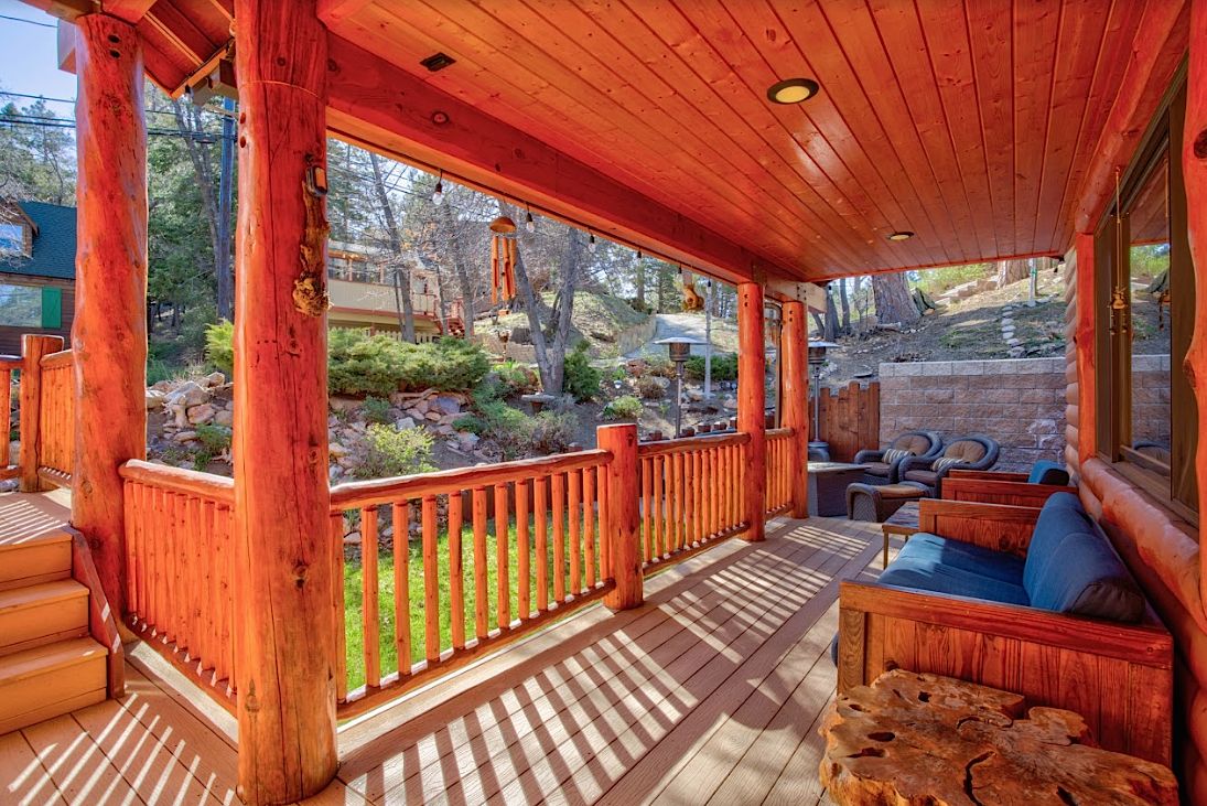 Wraparound porch with log railings, wooden bench seating, and forest views