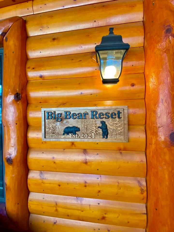 Carved wooden 'Big Bear Reset Est. 2021' sign with bears mounted on the log cabin wall
