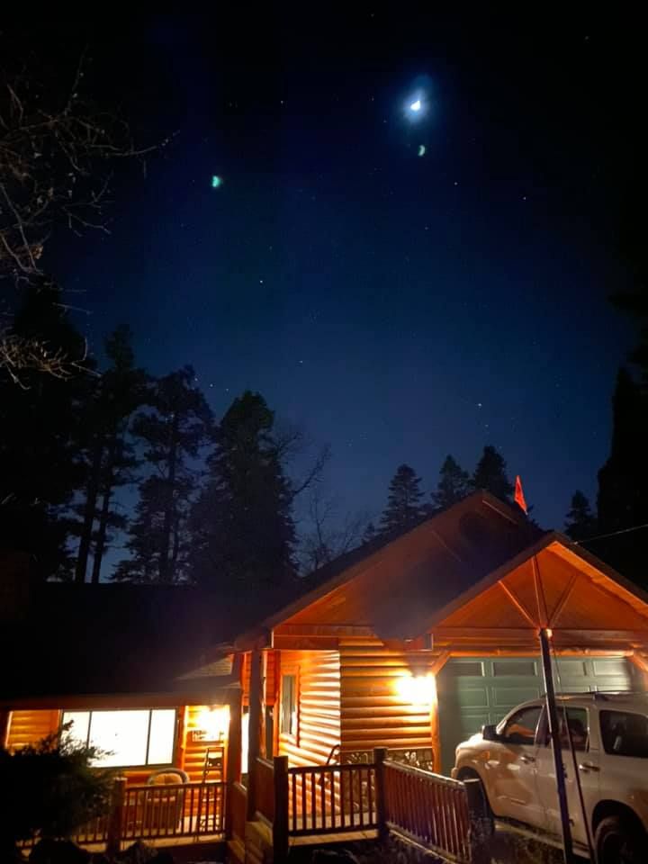 Log cabin glowing under a moonlit, starry night sky