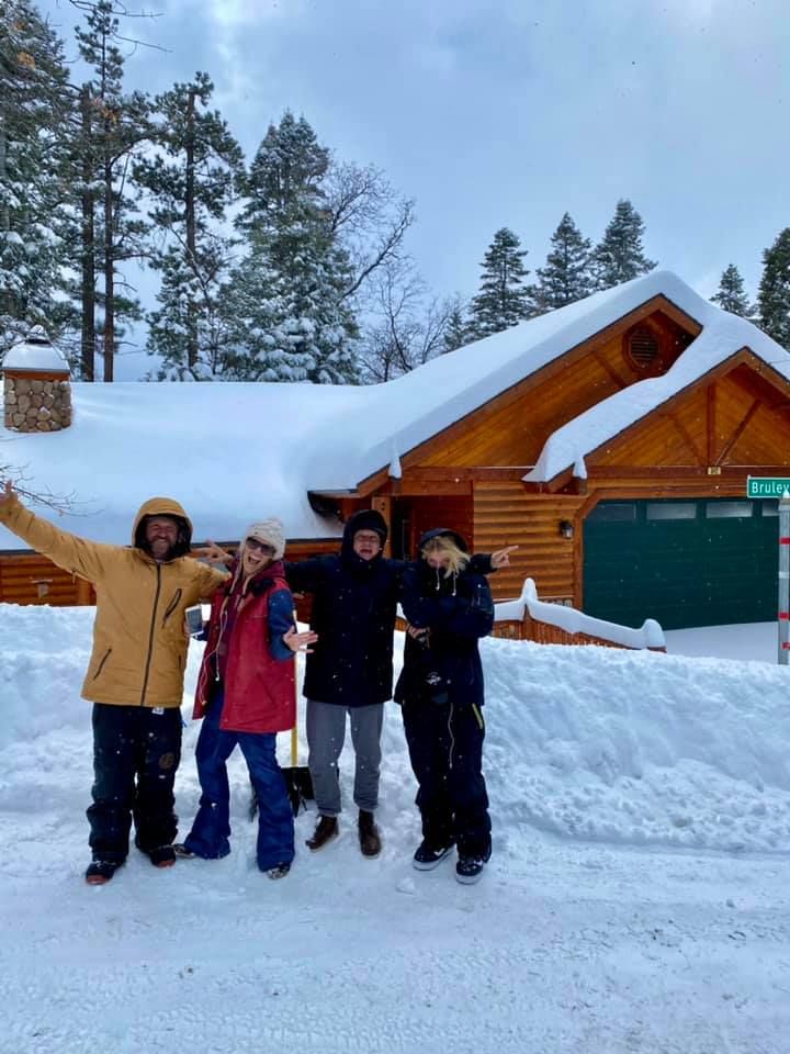 Happy guests in snow gear posing in front of the snow-covered cabin